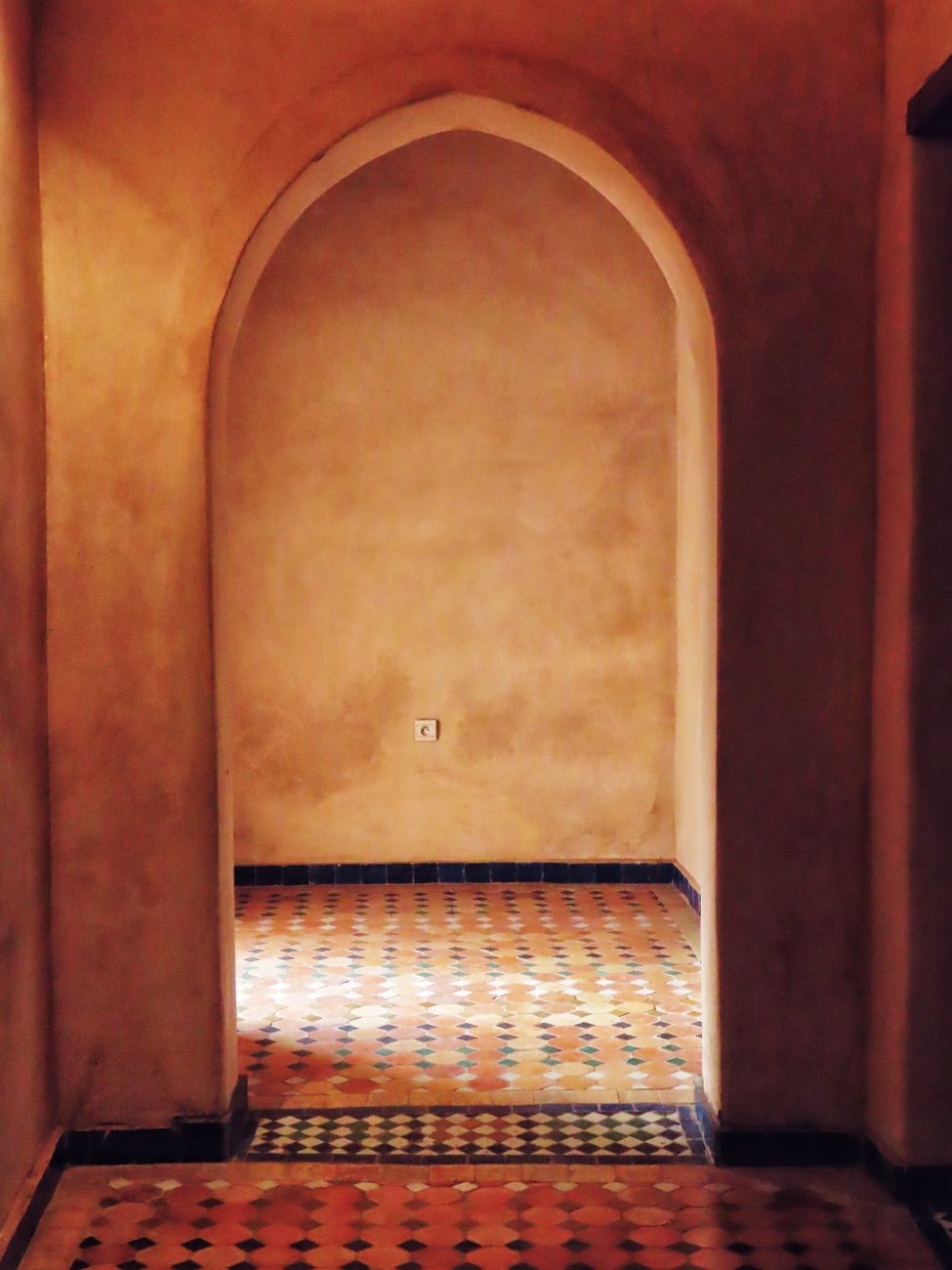A warm arched hallway with patterned tiled floors.