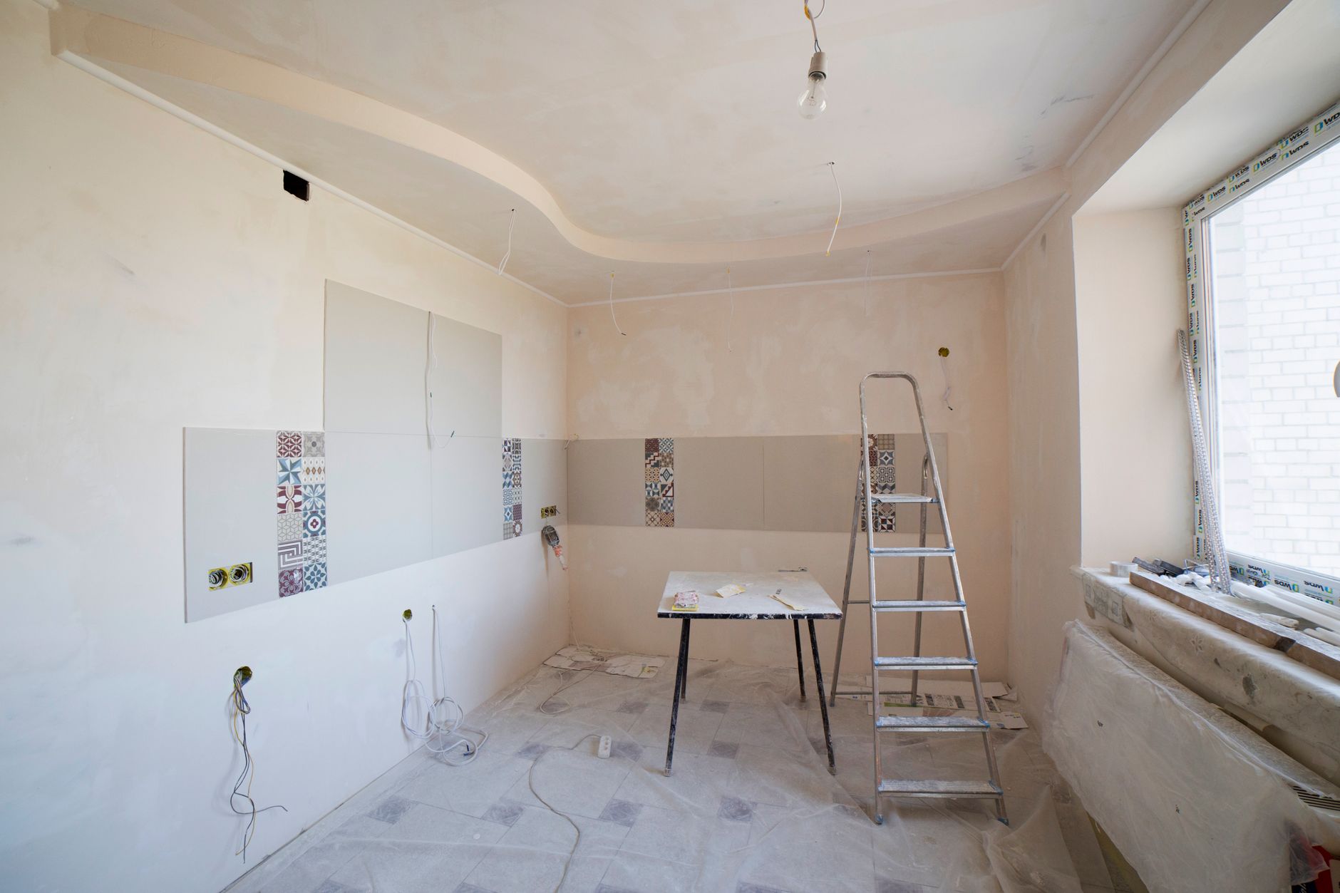 A kitchen under renovation: a ladder, tools and fresh plaster — the honest middle of a project.