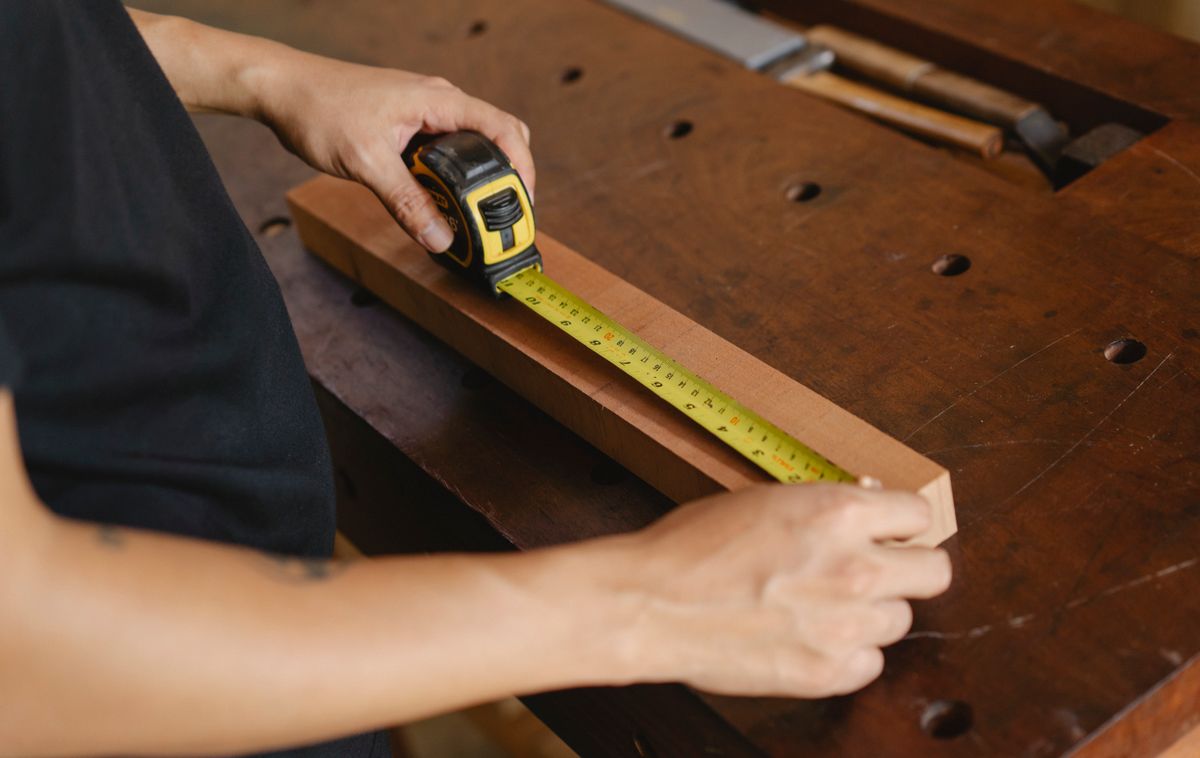 A craftsman measuring timber with a ruler at a workbench